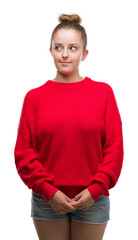 Wall Mural - Young blonde woman wearing bun and red sweater smiling looking side and staring away thinking.