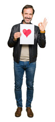 Canvas Print - handsome middle age man holding paper with red heart doing ok sign with fingers, excellent symbol