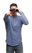 © Krakenimages.com - Handsome young man looking through binoculars pointing with finger to the camera and to you, hand sign, positive and confident gesture from the front