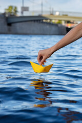 Wall Mural - A hand putting a paper boat into water, launch a paper boat on the river