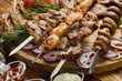Shashlik from different meats on barbecue skewers with vegetables and lavash on wooden board. Top view. Food background.