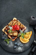 Tasty waffles with caramelized pear, berries, sweet sauce on black serving board on grey background. Dessert. Serving food