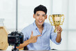 Young Asian businessman shows a golden trophy to the camera.
