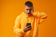 © fotofabrika - Young man expressing negativity while reading message on the mobile phone on yellow background