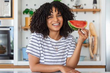 Wall Mural - Image of cheerful young woman eating watermelon in the kitchen at home