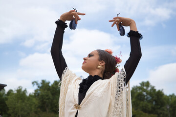 Poster - Portrait of young teenage girl in black dance dress, white shawl and pink carnations in her hair, dancing flamenco with castanets in her hands. Concept of flamenco, dance, art, typical Spanish dance.