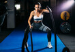 Fit beautiful woman with battle rope exercise in the fitness club.