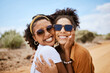 © S Fanti/peopleimages.com - Couple travel portrait, Dubai desert with summer sunglasses or care free tourism road trip together. Happy black women friends in outdoor vacation, smile on faces in natural sandy street on adventure