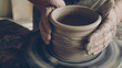 Senior male ceramist is concentrated on making pot from clay on spinning throwing wheel. He is correcting form of earthenware and finishing ornament.