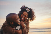 Love, Travel And Fun Couple At Beach Enjoying Summer Vacation Or Honeymoon At Sunset With A Piggy Back Ride While Being Playful. Laughing, Energy And Seaside Holiday With Black Man And Woman Together