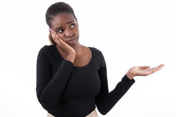 Wall Mural - Portrait of tired African American woman pointing with palm. Dreaming young model in black shirt with ponytail looking away, touching cheek and showing ads. Advertisement concept.