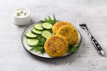 Delicious millet cutlets with carrots and seeds served with cucumber and herbs on a gray textured background, top view. Homemade vegan food