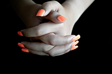 Selective focus of intertwined female hands with orange false nails, on black background. nail manicure