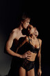 © LIGHTFIELD STUDIOS - young shirtless man embracing passionate tattooed woman in lingerie on black background.