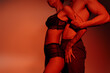 © LIGHTFIELD STUDIOS - partial view of sexy woman in black lace lingerie near shirtless man on red background.