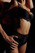 © LIGHTFIELD STUDIOS - partial view of man embracing young woman in lace underwear isolated on black.