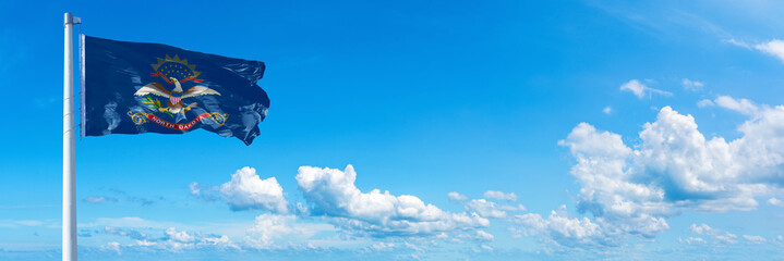 Wall Mural - North Dakota - state of USA, flag waving on a blue sky in beautiful clouds - Horizontal banner
