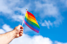 Man's Hand With An Unfurled Rainbow Flag On A Blue Background