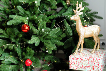 Wall Mural - Christmas decor. A golden deer stands next to a Christmas tree decorated with a garland and red balls