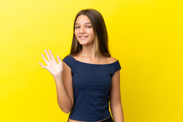 Sticker - Little caucasian girl isolated on yellow background saluting with hand with happy expression