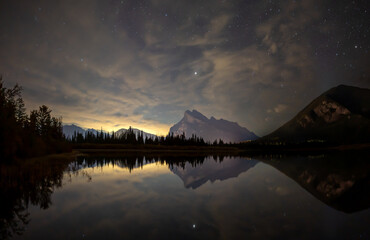 Wall Mural - peaceful night mountain scene with a peak reflecting in a calm and a sky with broken cloud and stars