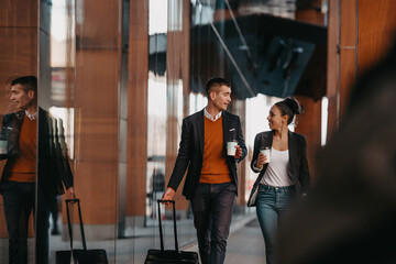 Business man and business woman talking and holding luggage traveling on a business trip, carrying fresh coffee in their hands.Business concept