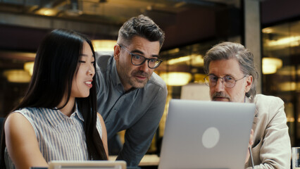 Multi-ethnic office coworkers having business meeting in modern office, using laptop. Businesspeople working on startup project. Discussion of company strategy