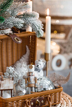 Cozy Winter Concept. Home Warmth In Cold, Frosty Weather. Still-life. Christmas Toys, Wicker Basket, Candles And Fir Branches On The Coffee Table In The Living Room Home Interior.