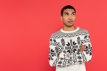 Wall Mural - thoughtful african american man in warm sweater standing with crossed arms and looking away isolated on red