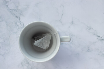 Tea bag in cup on white marble table background. Top view, copy space. Teabag in empty mug. Teatime concept