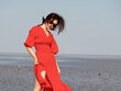 Sexy Chinese young girl in red dress posing on sunny beach with black long hair in wind. Emotions, people, beauty and lifestyle concept.