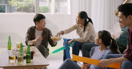 Wall Mural - Group of young adult friend man and woman asia people sit at sofa couch joy chanting party fun game FIFA world cup live TV at home eat snack bowl drink beer bottle glass jump mad happy win exult face.