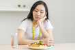 © KMPZZZ - Diet in bored face, unhappy beautiful asian young woman on dieting, looking at salad plate on table, dislike or tired with eat fresh vegetables. Nutritionist of healthy, nutrition of weight loss.