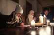 © weyo - Girl in winter hat and shawl studies at home at the table by candle lights while fanily experiences winter power blackout