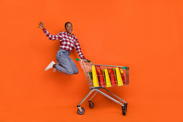 Wall Mural - Full length of crazy energetic girl jumping have fun enjoy free time shopping isolated on orange color background