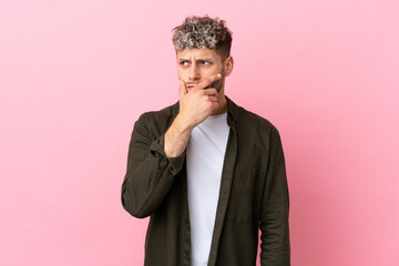 Wall Mural - Young handsome caucasian man isolated on pink background having doubts and with confuse face expression