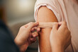 © Kay Abrahams/peopleimages.com - Covid, vaccine and plaster with a doctor and patient consulting in an appointment or checkup at home. Nurse, healthcare and trust with a health professional using a bandaid on an arm after medication