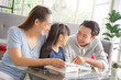 © aekkorn - Children education and home school concept : Young asian father and mother see little daughters' study. Excited smiling small child girl enjoying learning and reading with pleasant dad and mom at home