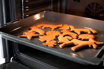 Close up Christmas gingerbread on a baking sheet in open modern oven in a bright kitchen. Christmas cookies in the oven - warm light, festive atmosphere. Concept of winter, Christmas, and New Year