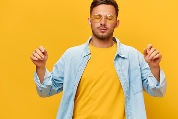 Wall Mural - Joyful dancing happy tanned handsome man in blue shirt sunglasses enjoy cool mood posing isolated on orange yellow studio background. Copy space Banner Mockup. Holiday concept