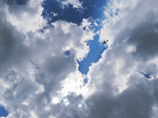 Wall Mural - The passenger airplane is flying far away in the blue sky and clouds. Dramatic clouds with the sun shining through them. Aircraft in the air. International passenger air transportation