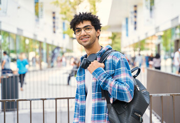 Young curly middle eastern smiling man with braces  standing on the street. Portrait of happy tourist with backpack looking at camera. Travel concept 