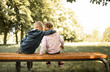 Little brother and sister, girl and boy sitting on park Bench together. Family love concept. 