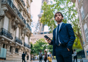 Holidays in Paris. Man in a suit using her smartphone in Paris, France. European worker. Street with Eiffel Tower view.