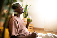 Relaxed Black Man Drinking Green Smoothie At Home. Side View Of African American Man Enjoying Healthy Juice.
