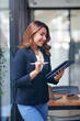 © amnaj - Attractive smiling Asian businesswoman standing holding tablet working and recording work details in office.