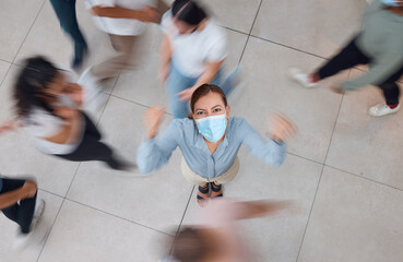 Angry business woman with a mask for covid and people walking around her. Young girl wearing face mask in a crowd, frustrated and shaking her fist. Aerial view of upset female in mall or office