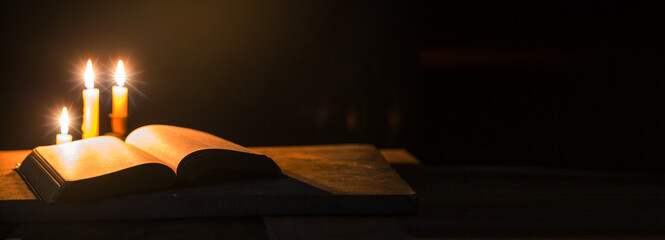 Wall Mural - Light candle with holy bible and cross or crucifix on old wooden background in church.Candlelight and open book on vintage wood table christianity study and reading in home.Concept of christ religion