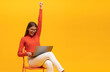 © Damir Khabirov - Excited young woman sitting on chair with laptop, shouting yes as winner, isolated on yellow