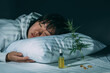 Asian girl sleeping in evening bedroom with cbd oil, capsules and a cannabis branch. Melatonin production, concept of combat sleep disorders. Dark background